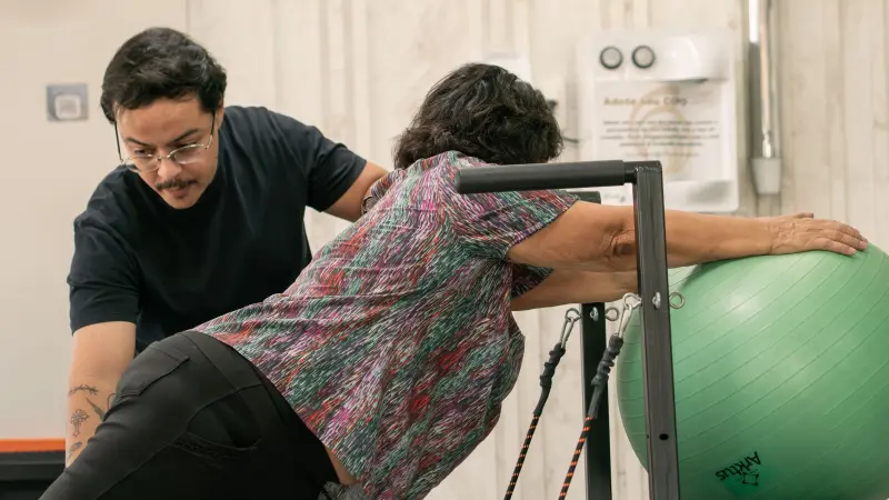Fisioterapeuta orientando paciente idosa em alongamento de tronco apoiada em bola suíça
