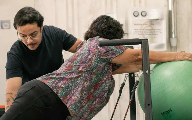 Fisioterapeuta orientando paciente idosa em alongamento de tronco apoiada em bola suíça