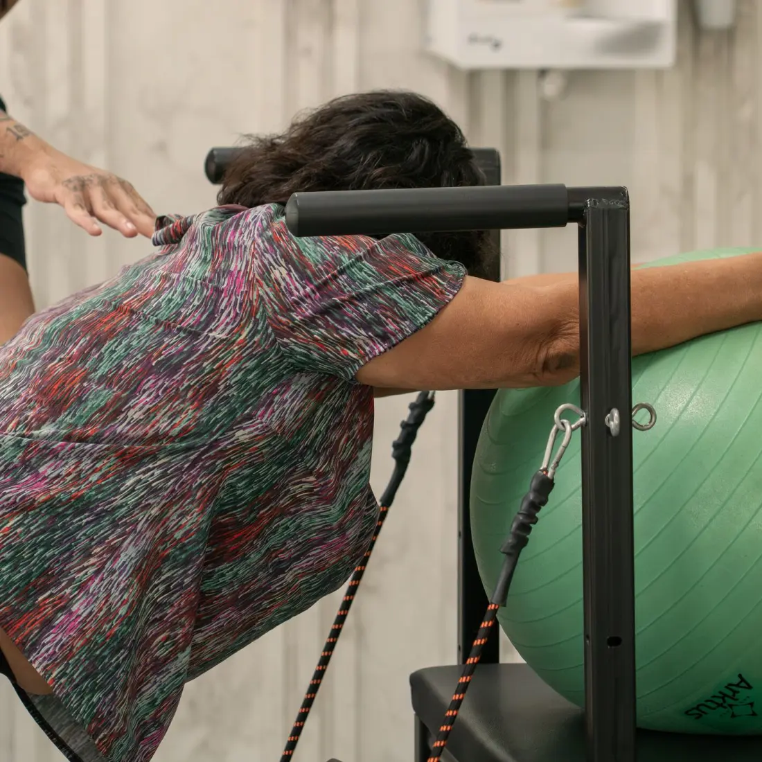 Paciente idosa alongando o tronco sobre bola suíça verde com fisioterapeuta ao lado