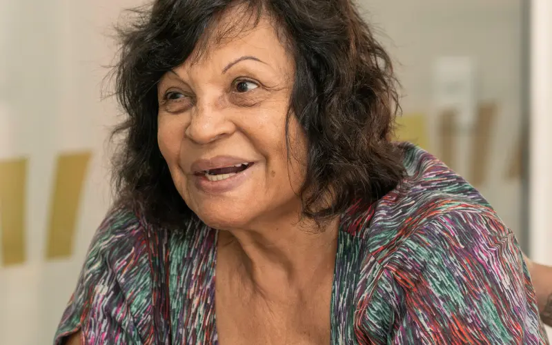 Paciente idosa sorrindo durante conversa na clínica, com fundo claro desfocado
