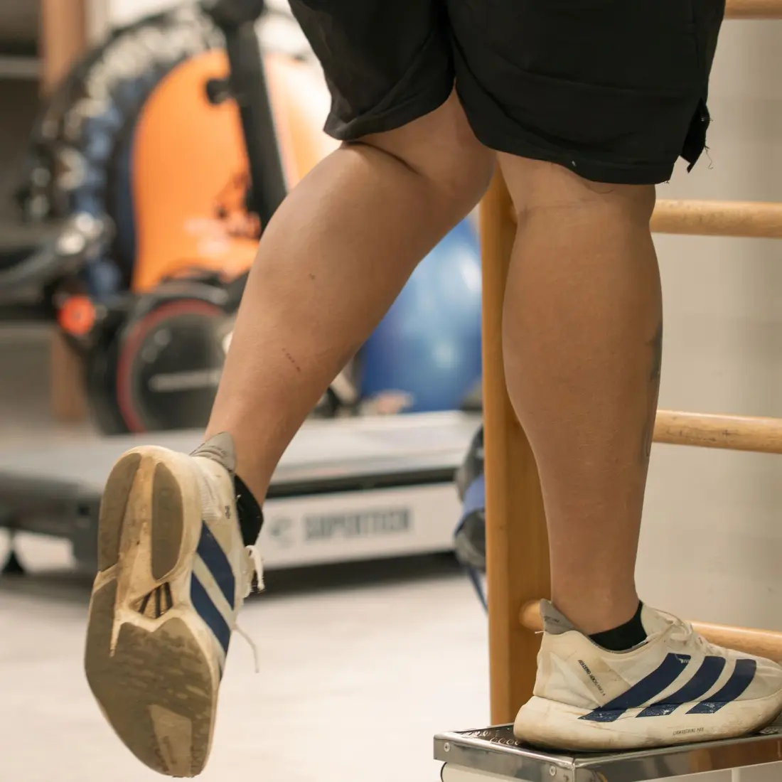 Paciente sobe em step junto ao espaldar em exercício de fortalecimento de membros inferiores