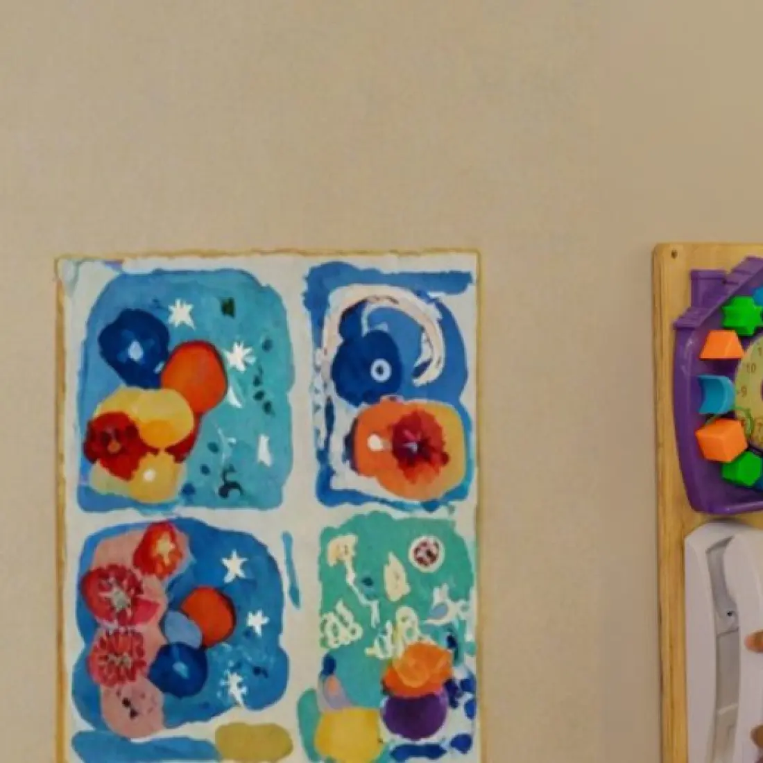 Criança brinca no painel sensorial ao lado de desenhos na parede