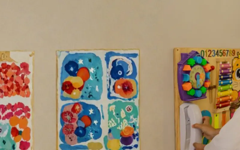 Criança brinca no painel sensorial ao lado de desenhos na parede